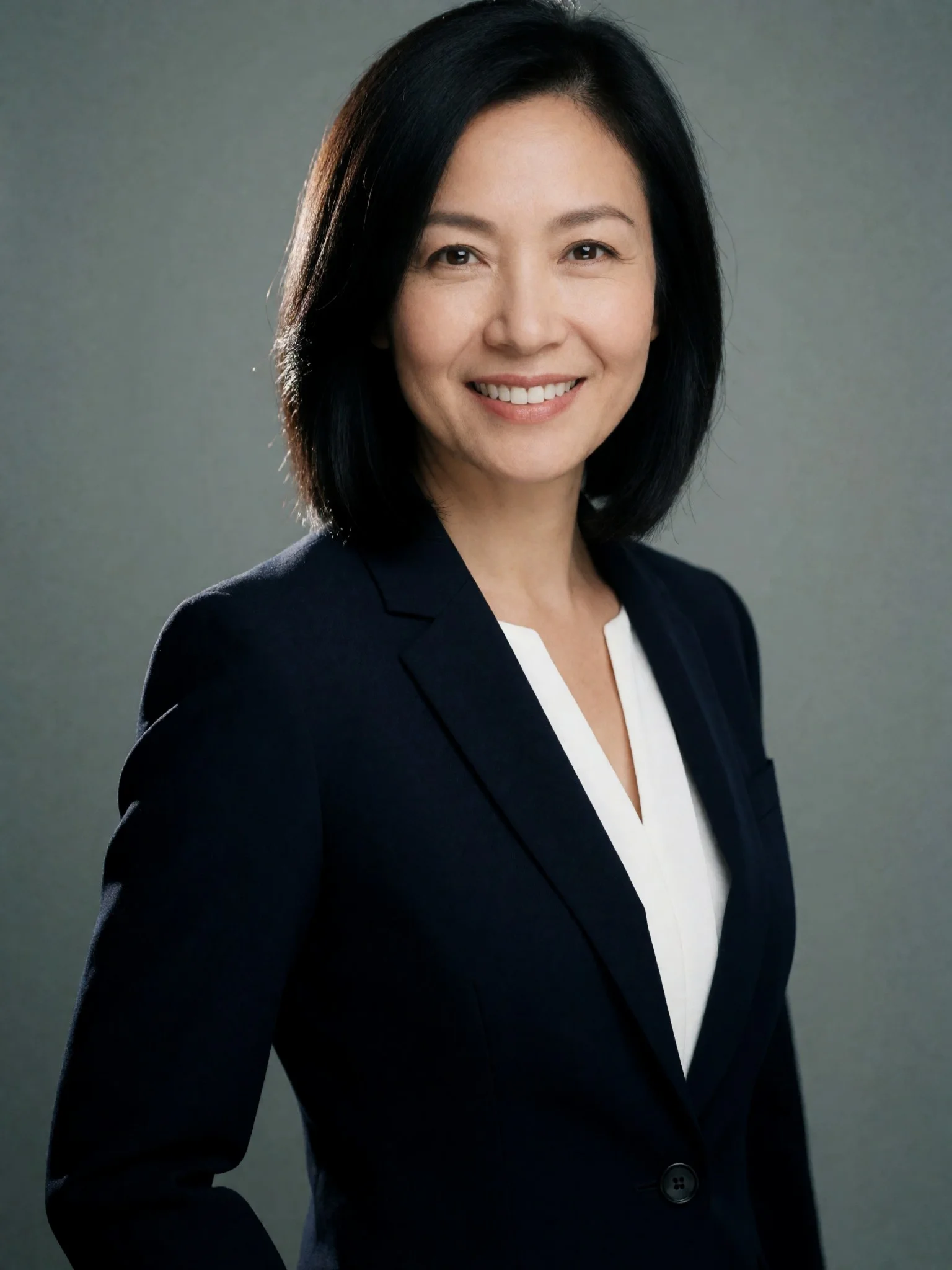 Sample professional portrait of a woman in a navy blazer and white blouse against a neutral grey background.